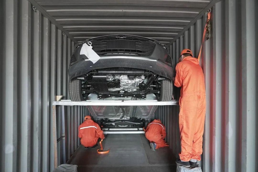 Workers lashing a car on a two-tier rack inside a shipping container